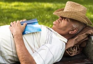 Man resting in a field with his hat pulled down and a book on his chest